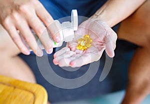 Close up photo of one round yellow pill in hand. Man takes medicines with glass of water. Daily norm of vitamins, effective drugs,