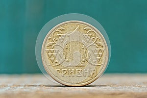 One round yellow Ukrainian hryvnia coin on a gray table on a green background