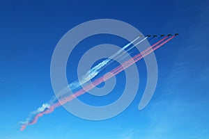 One row formation of a group of six russian military fighter jet planes flying high in blue sky and leaving a blue white red smoke