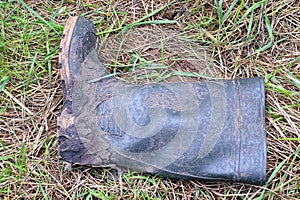 One rubber dirty green boot in the mud