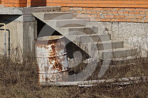 Rusty old barrel stands in dry grass near the house with a ladder