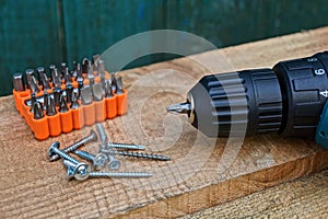 One screwdriver with a set of bits in a plastic box in a pile of screws on a wooden table