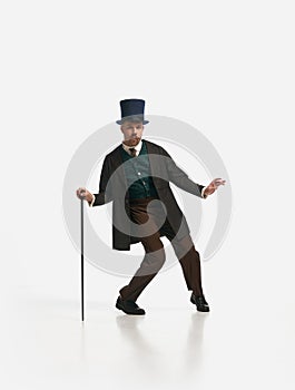 One serious man wearing old-fashioned clothes and vintage hat dancing with cane over white background. Time to entertain