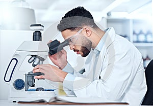 One serious young male medical scientist sitting at a desk and using a microscope to examine and analyse test samples on