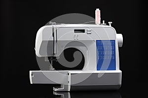 One sewing machine with spool of thread on black background