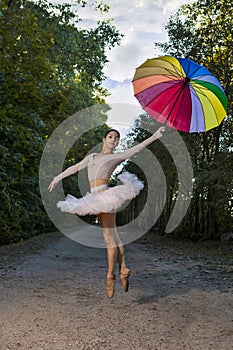 One Sexy Winsome Caucasian Ballet Dancer in Rose Pink Tutu Posing With Colorful Umbrella During Ballet Pas Jumping in Summer