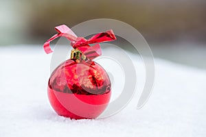 One shiny red christmas ball outside in snow