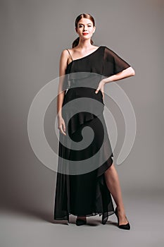 One shoulder ruffled maxi dress in black. Asymmetric open-back chiffon gown with a strap, split and frills. Beautiful young lady p photo