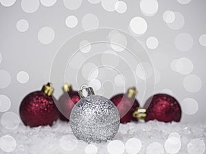 One silver ball on the Christmas tree and four red balls in the back, on a bokeh background