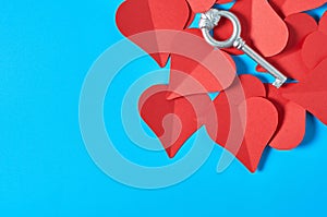 One silver vintage key on heap of red paper hearts lies on blue countertop. Concept of closed or opened love or Valentines day