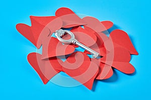 One silver vintage key on heap of red paper hearts lies on blue countertop. Concept of closed or opened love or Valentines day