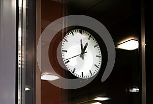 One single backlit clock on a darkened train station platform, public area object closeup detail. Commute transportation rush hour