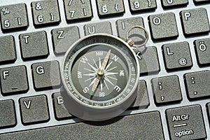 One single compass laying on a modern computer desktop PC keyboard, world navigation, different directions, NSWE object closeup,