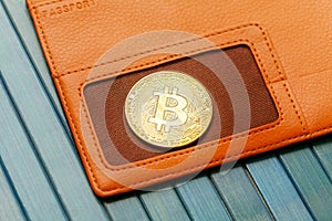 One single gold bitcoin coin symbol laying on an orange wallet, object closeup, detail, nobody. Crypto currencies storing