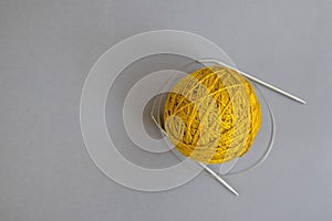 One skein of yellow wool yarn and knitting needles on an gray background, handmade, knitting. Close-up. Copy space.