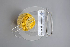 One skein of yellow wool yarn, knitting spokes, measuring ruler and large pin on gray background, handmade, knitting. Close-up.