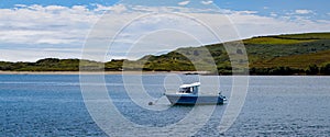 One small fishing boat on a calm water surface near the hilly Irish coast on a sunny summer day. boat on body of water