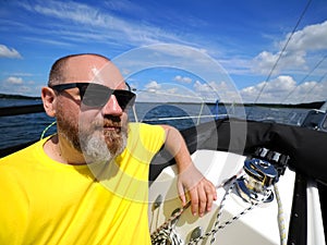 One smiling bearded adult man sailing on a sailboat during his yacht voyage in a sunny summer day