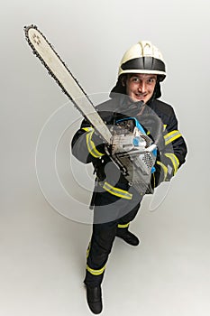 One smiling male firefighter dressed in uniform posing with saw over white studio background.