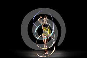 One sportive emotional girl, rhythmic gymnastics artist isolated on dark background in ray of light. Concept of sport