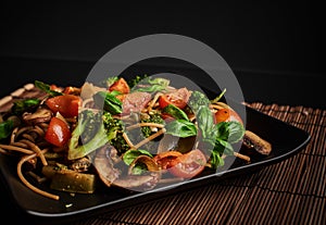 One square plate with Italian vegan integral pasta with broccoli, mushrooms, cherry tomatoes and basil leaves - vegetarian dish