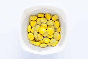 One squared small bowl with small yellow sugar coated chocolate candies isolated on white background, top view or flat lay of swee