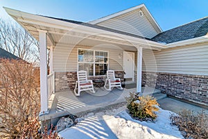 One storey home with rocking chairs on porch overlooking snowy winter scenery