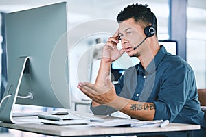 One stressed and confused hispanic call centre agent talking on headset while working on broken computer in an office