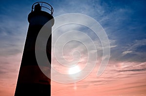 One striped lighthouse stand on the beach in the city of Faro in Portugal. Little waves in the ocean on a dark evening .