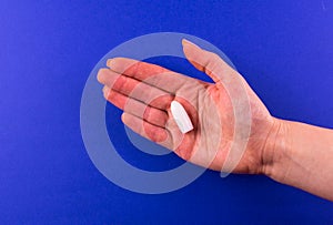 One suppository for anal or vaginal use in a female hand on a blue background. Medical candles. Copy space.