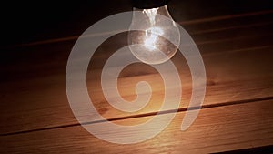 One Swinging Glowing Incandescent Light Bulb in Thick Smoke on Wooden Background