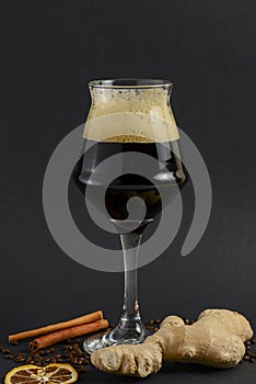 One tall glass of cold dark craft beer with spices over black background. Hops, anise, cinnamon, ginger. Copy space