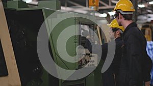 One technician or worker explain how to operate big machine to his co-worker with blue uniform with yellow helmet in the factory