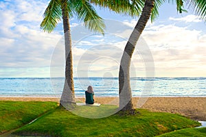 One teenage girl sitting alone on Hawaiian beach watching ocean