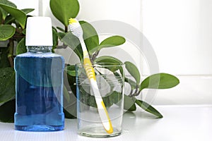 One toothbrushe in a glass cup and a mouthwash on the bathroom table against a background of green foliage