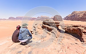 One tourist with his local guide looking at the stone arch in the desert of wadi rum in Jordan. Blue sky