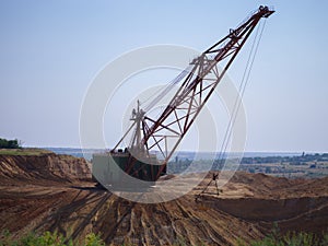 One-tower metal mobile crane on a blue sky background. An industrial moving machine in the sandy quarry. Copy space.