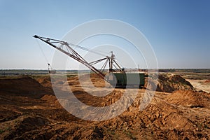One-tower metal mobile crane on a blue sky background. An industrial moving machine in the sandy quarry. Copy space.