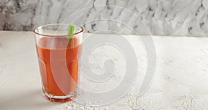 One transparent glass cup with red tomato juice and a sprig of celery on a light background. Healthy food concept.