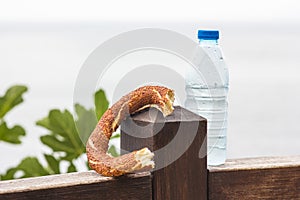 One Turkish bagel simit and watter bottle laid on a wooden surface, close-up