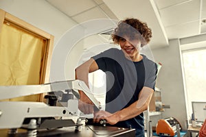 One. Two. Three. Done. Young cheerful male worker using heat press transfer machine for printing t-shirt at workplace