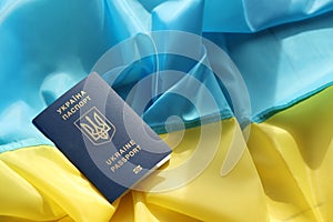 One Ukrainian biometrical passport on folded waving flag of Ukraine country