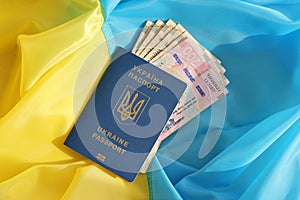 One Ukrainian biometrical passport and UAH hryvnia bills on folded waving flag of Ukraine