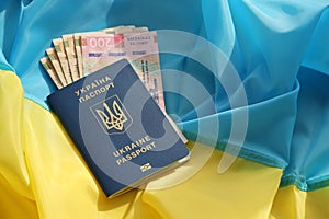 One Ukrainian biometrical passport and UAH hryvnia bills on folded waving flag of Ukraine