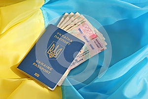 One Ukrainian biometrical passport and UAH hryvnia bills on folded waving flag of Ukraine