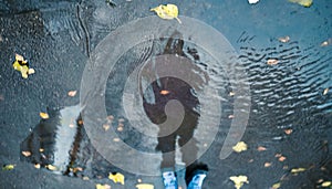 One unrecognizable person blurry silhouette as reflection in a puddle on wet city street during rainy day