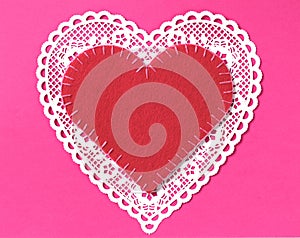 One Valentines Day Heart made of a white doilie with a red stitched, handmade felt heart, all on a bright pink paper with space in