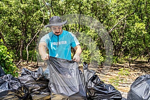 One volunteers in work overalls collect garbage in forest in plastic bag. Close-up during action. Cleaning of nature from waste.