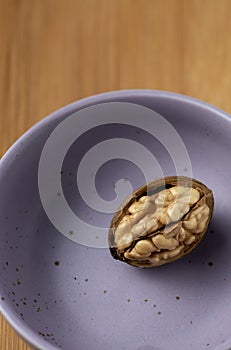 One walnut in a violet plate on a wooden background on top view Still life photography