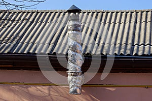 One warmed long metal pipe on a gray slate roof against a blue sky